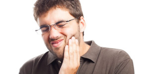 Mann hält sich die Wange vor Zahnschmerzen