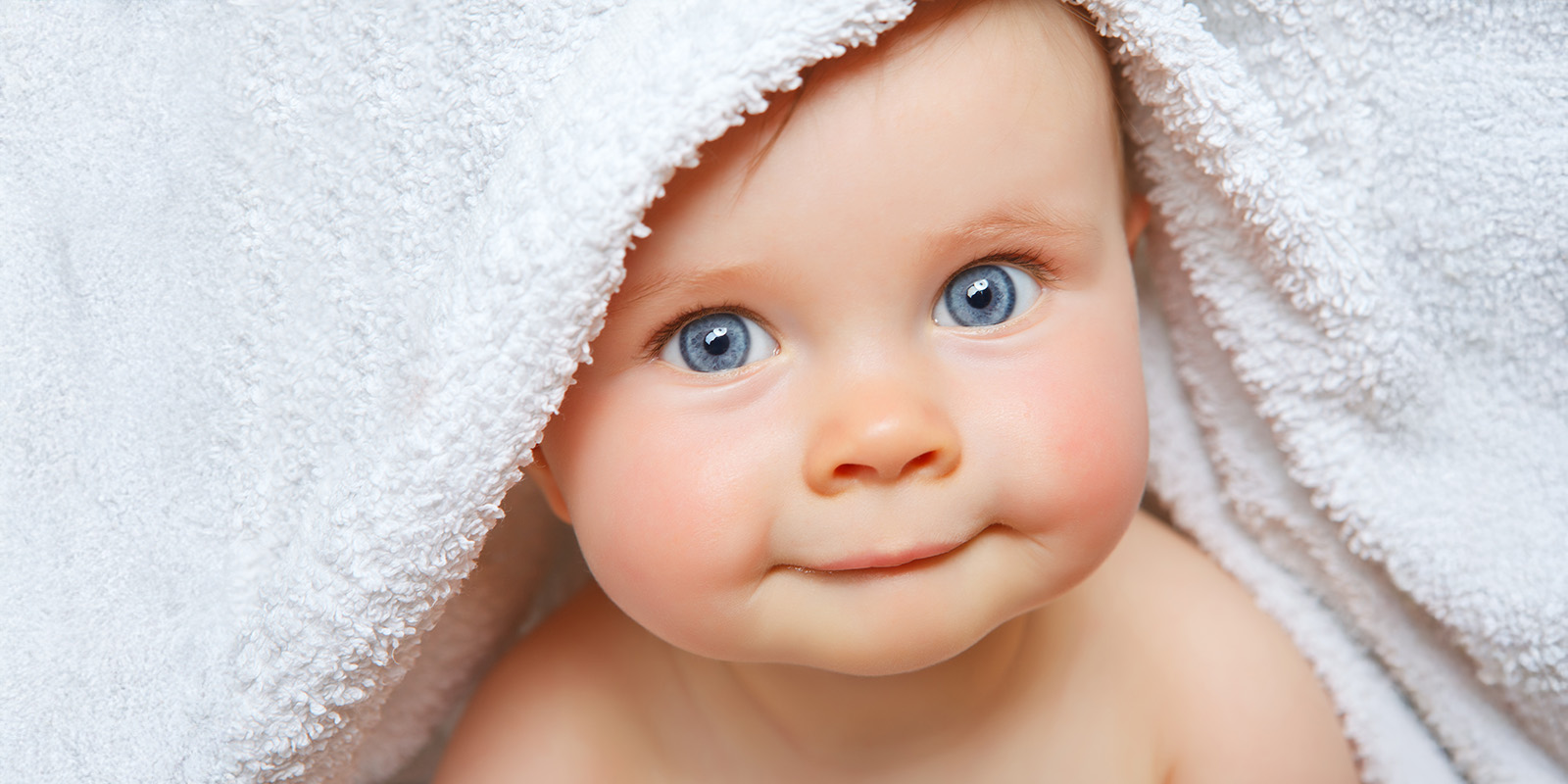 Kleines Baby schaut unter weißem Handtuch hervor.