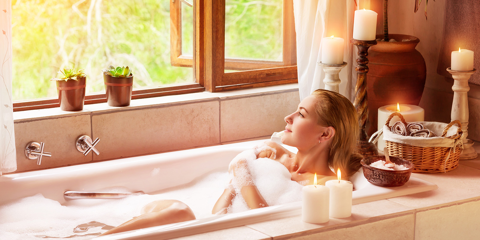 Eine freu liegt in der Badewanne und richtet ihren Blick aus dem Fenster. Um die Badewanne herum sind Kerzen aufgestellt.