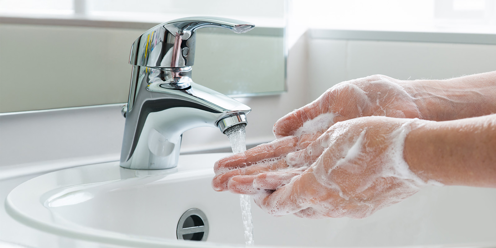 haendewaschen-seife-haende-waschbecken Eingeseifte Hände werden über einem Waschbecken mit laufendem Wasserhahn gewaschen.