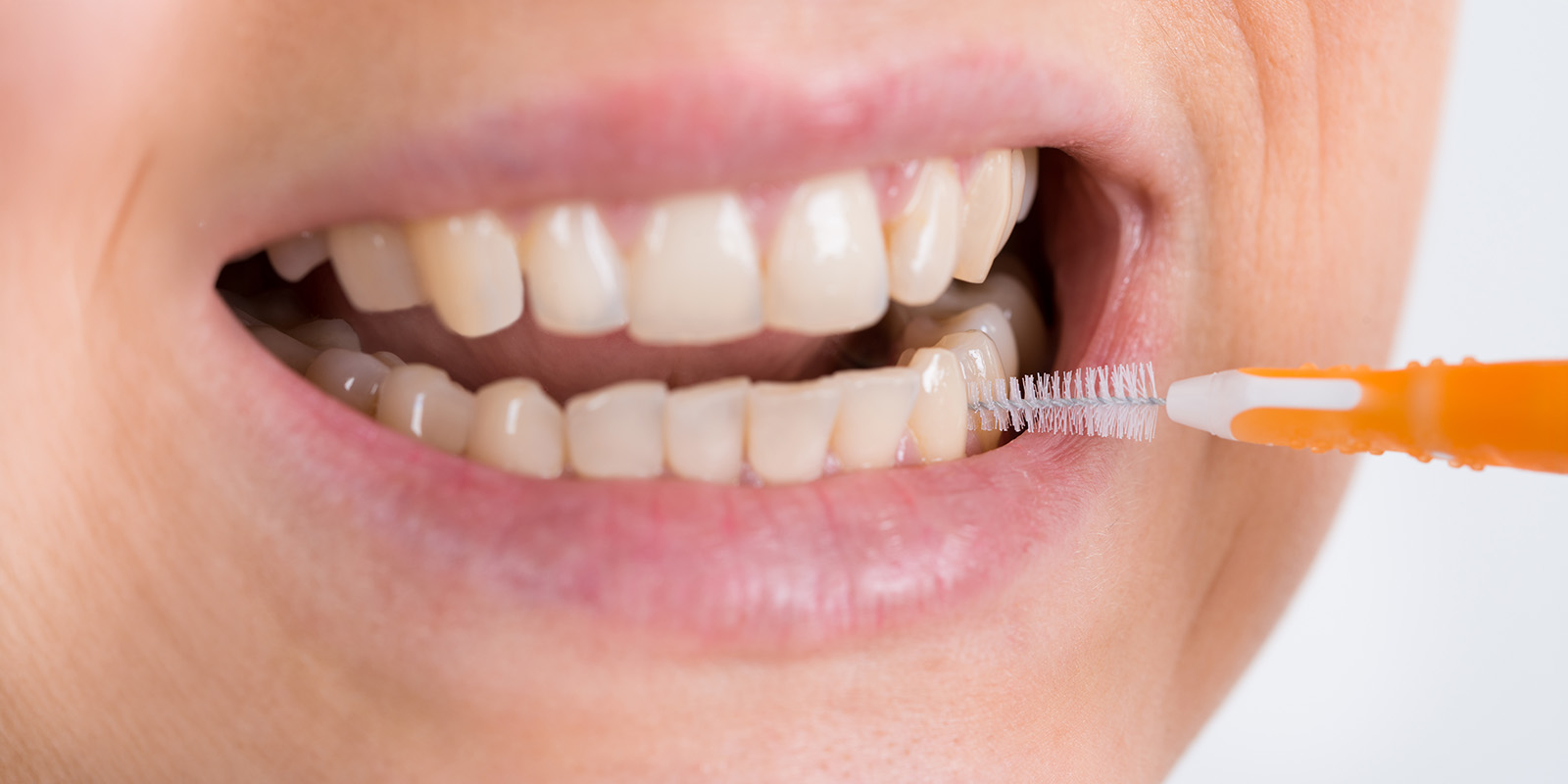 EIne Person wendet eine Interdentalbürste bei ihren Zähnen an.